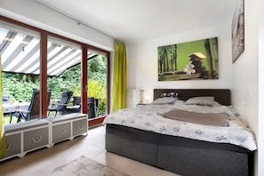 Un dormitorio con cama, ventana con cortinas, un cuadro y vista a zonas verdes.