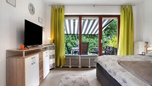 A bedroom with a bed, a TV, a dresser, a window with curtains, and a view of an outdoor patio. - Apartment 'Ferienpark Gustow B09' with Shared Terrace and Shared Garden (Gustow)