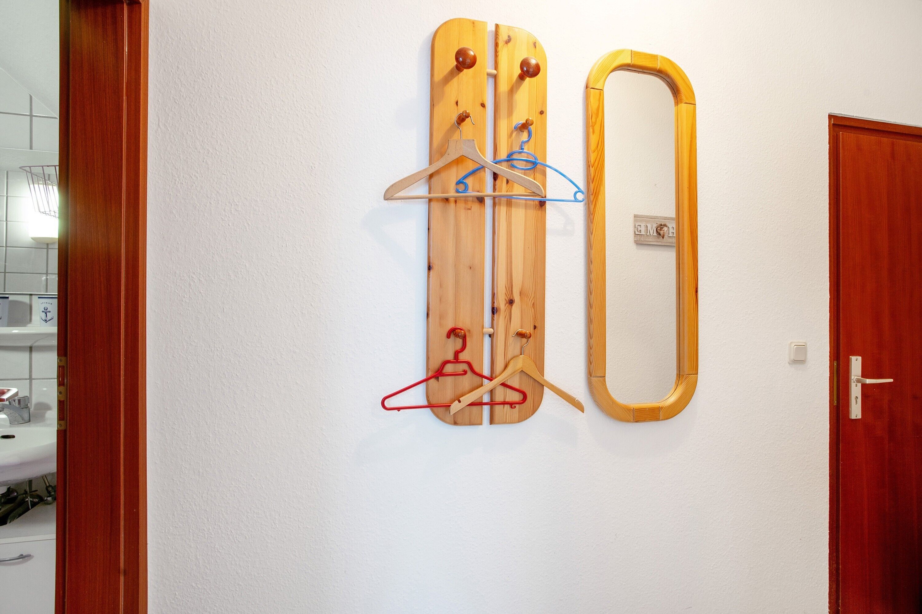 A wall-mounted wooden hanger board with multiple hangers and a mirror.