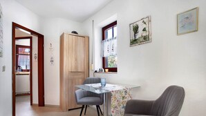 A compact kitchen with a wooden cabinet, a glass table with a floral tablecloth, and a gray chair. - Apartment 'Ferienpark Gustow B09' with Shared Terrace and Shared Garden (Gustow)