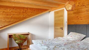 Ein Schlafzimmer mit schrägen Wänden, einem Bett mit floralem Bettbezug, einem Sessel und einer Pendelleuchte.