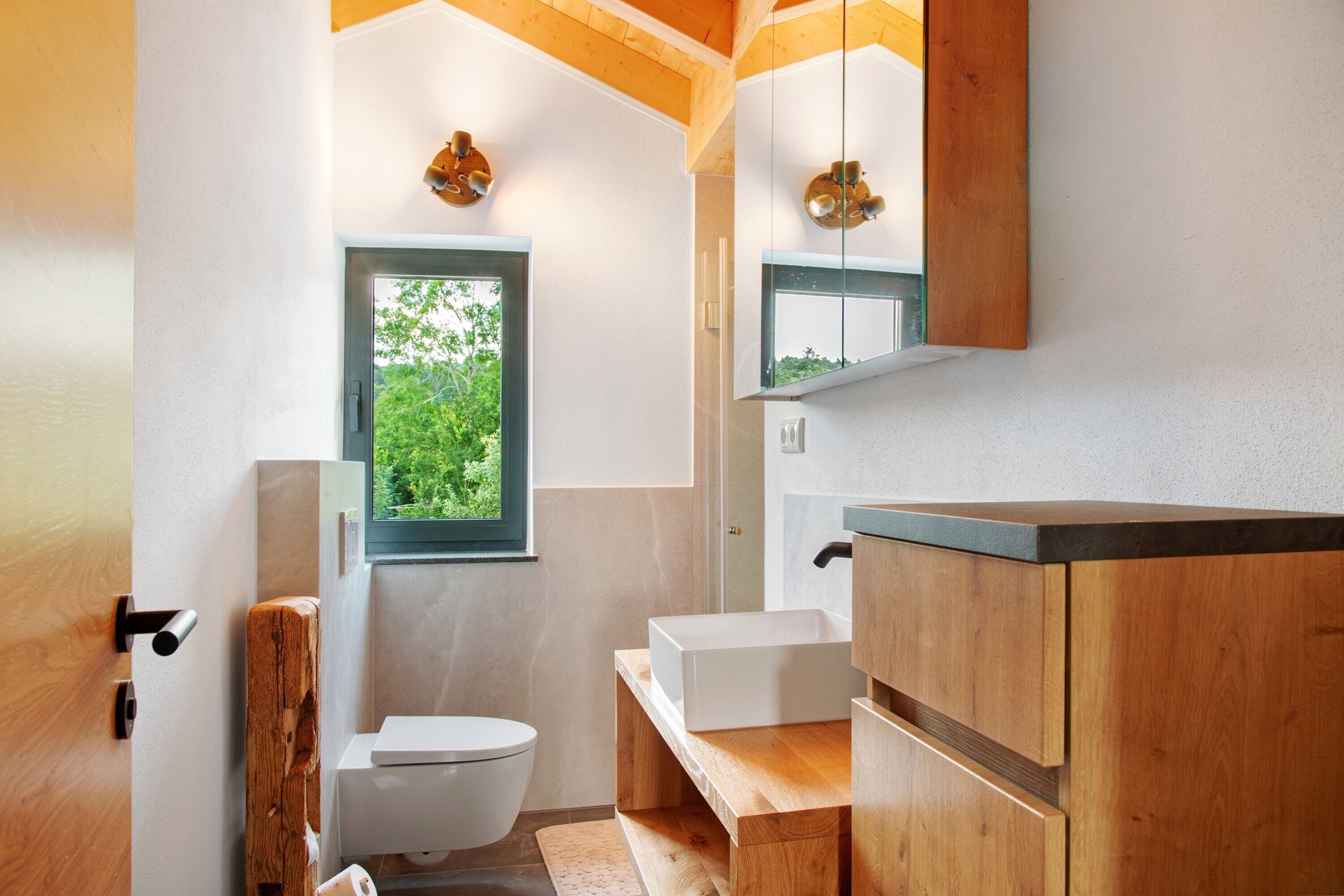 Een moderne badkamer met een houten wastafel, een witte wasbak en een raam met uitzicht op groen.