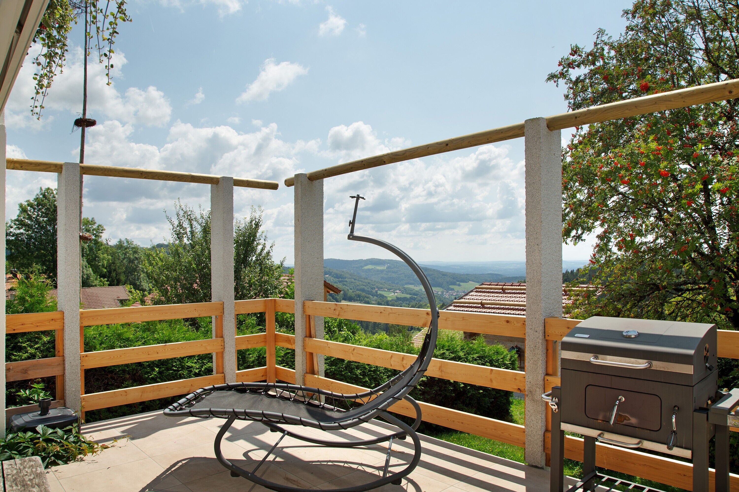 Un balcon doté d’une balustrade en bois, d’une chaise d’extérieur noire et d’un barbecue.