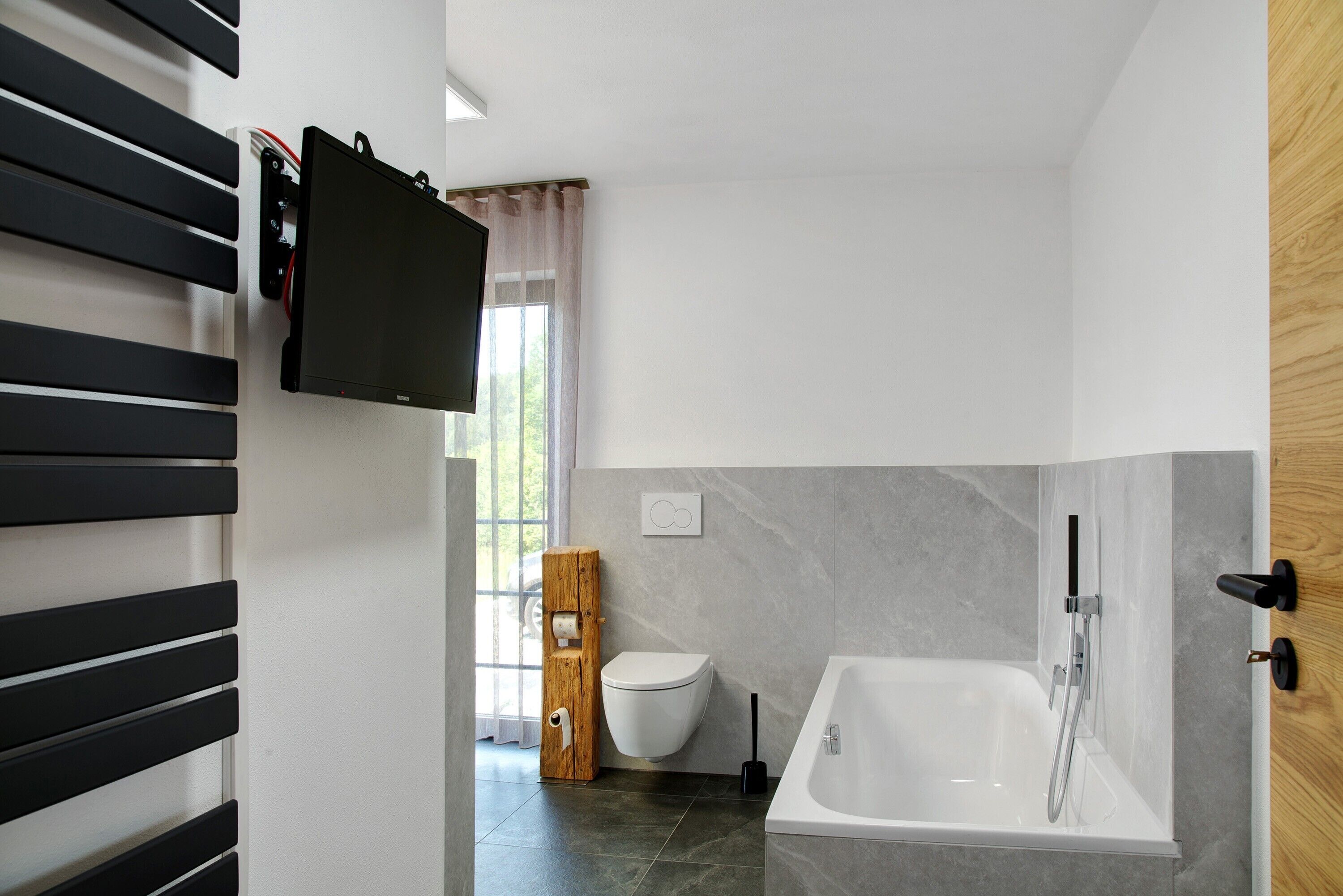 Ein modernes Badezimmer mit Toilette, Badewanne und einem an der Wand montierten Fernseher.