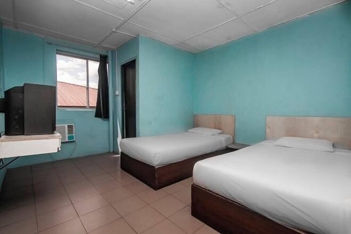 Une chambre avec deux lits, un bureau et une fenêtre donnant sur un immeuble.