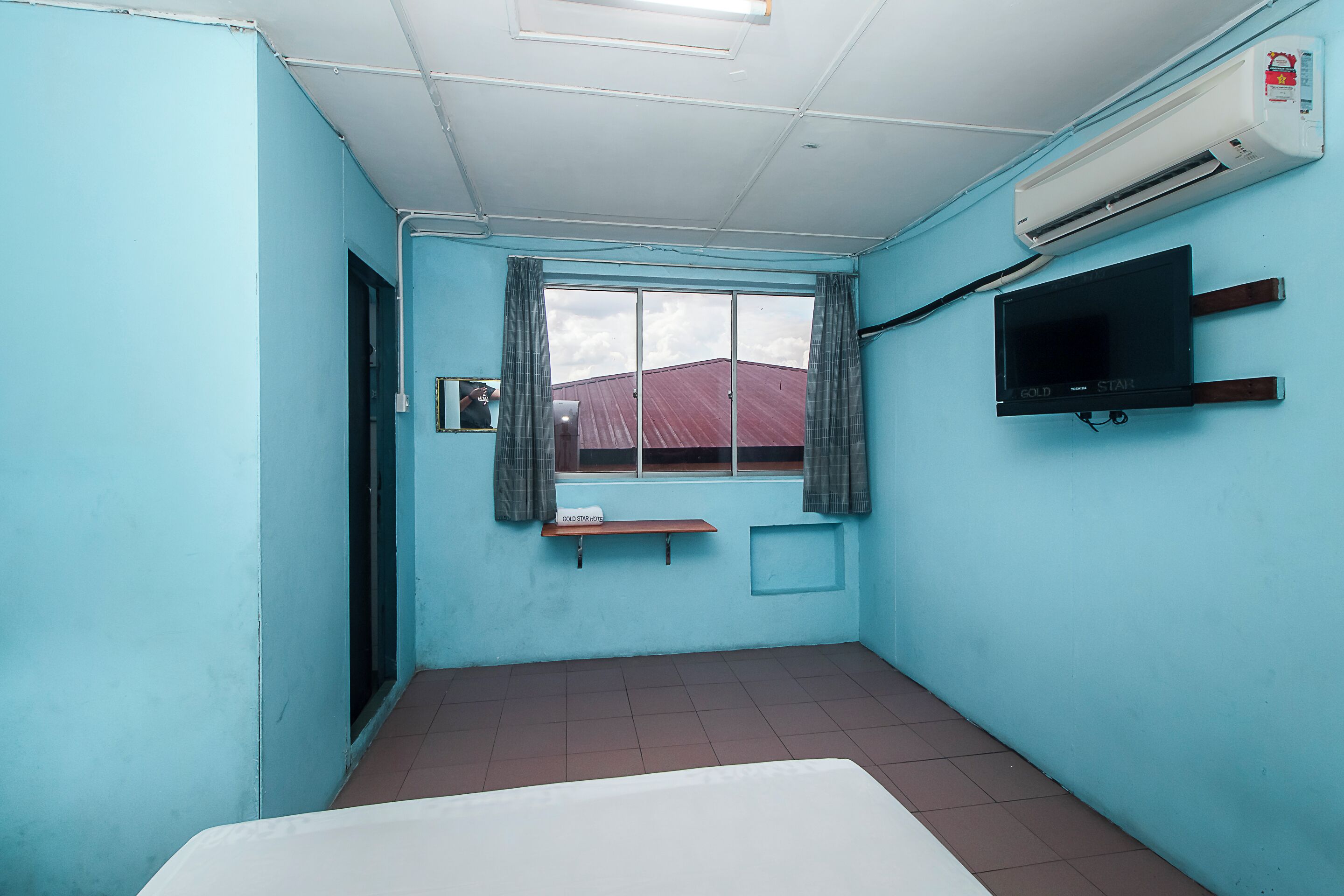 A room with a bed, a window with curtains, a mounted TV, and an air conditioning unit.