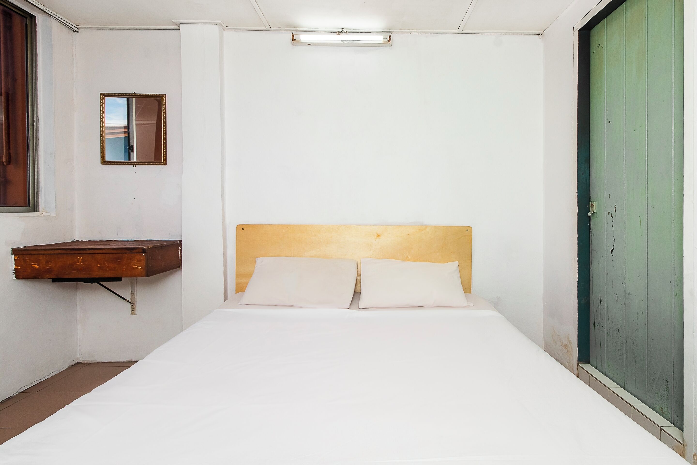 A single bed with a wooden headboard, a small bedside table, and a mirror on the wall.
