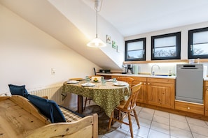 A dining area with a round table, chairs, a wooden bench, and a kitchen in the background. - Apartment 'Ferienwohnung Möwe' with Shared Garden and Wi-Fi (Friedrich-Wilhelm-Lübke-Koog)