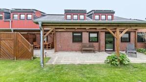 Une maison en briques avec un patio couvert, une clôture en bois et une allée gravillonnée.