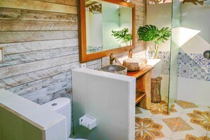 Une salle de bain avec un mur en bois, un lavabo avec un receveur en pierre, un miroir et un espace douche avec des carreaux à motifs.