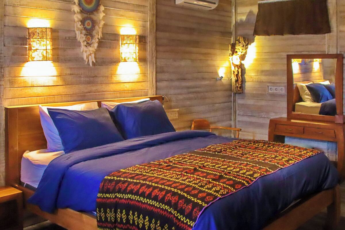 Ein Zimmer aus Holz mit einem Bett, zwei Wandleuchten, einem Spiegel und einer Klimaanlage.