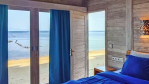 Une chambre avec un lit, une table de chevet et une vue sur la plage, accessible par une porte coulissante.