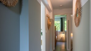 Ein modern gestalteter Flur mit hellblauer Wand, einer Wanddekoration und Blick in einen Raum mit Bett und kleinem Tisch.