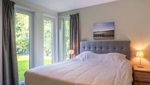 Ein Schlafzimmer mit einem großen Bett, zwei Nachttischen mit Lampen, einem Fenster mit Vorhängen und einem Bild an der Wand.