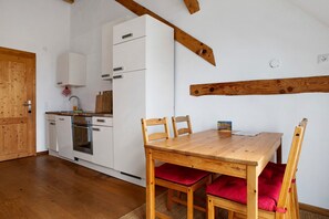 Eine Küche mit weißen Geräten, einem Holzespeisetisch mit roten Kissen und sichtbaren Holzbalken an der Decke.