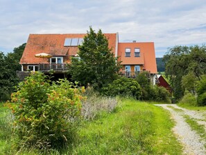 Una casa a due piani con tetto in tegole rosse, un balcone e un vialetto ghiaioso che conduce all'ingresso.