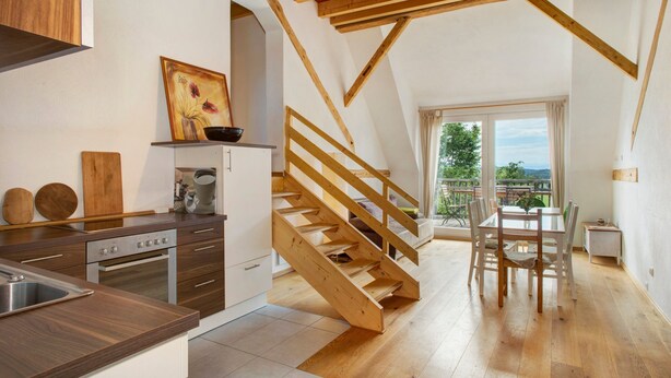 Una cocina moderna con vigas de madera, una zona de comedor con mesa y sillas, y vistas a través de un ventanal.