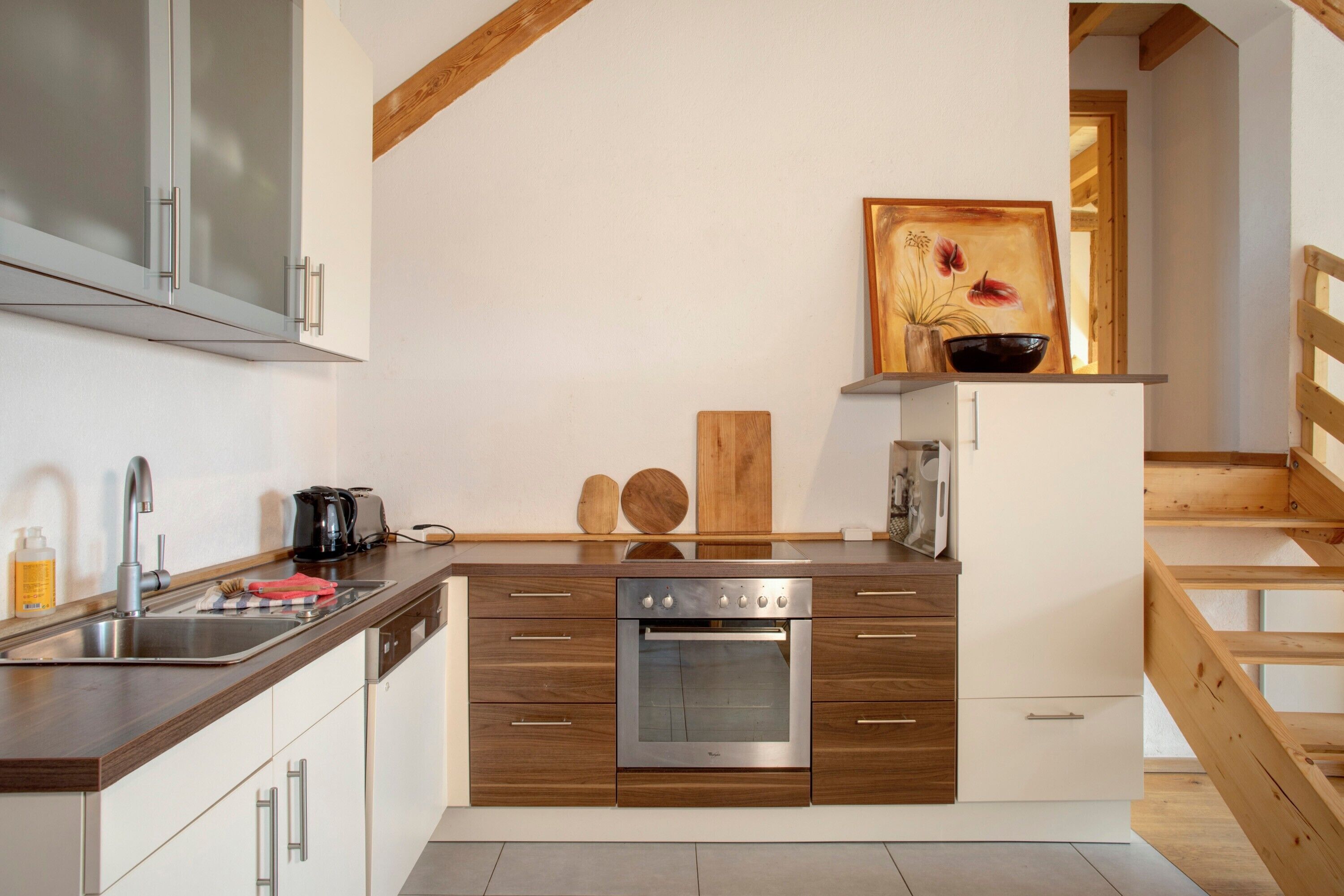 Een moderne keuken met een ingebouwde oven, een RVS-spoelbak en houten keukenkastjes.