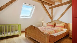 Una habitación con una cama de madera, una cuna, un ventanal y una pared roja.