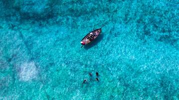 A boat on clear turquoise water with three people swimming nearby.