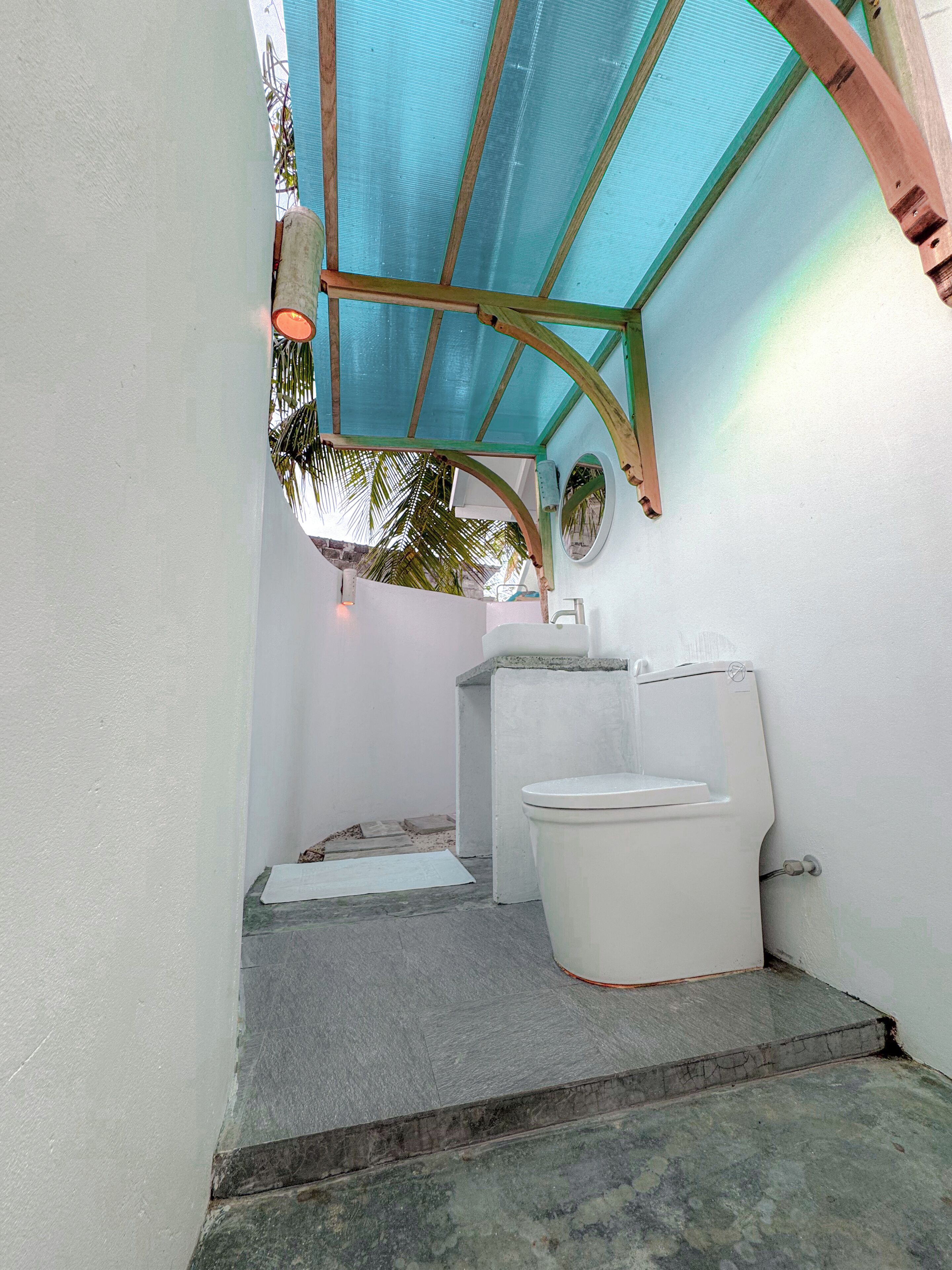 A small, enclosed bathroom with a toilet, sink, and a shower area with a blue ceiling.