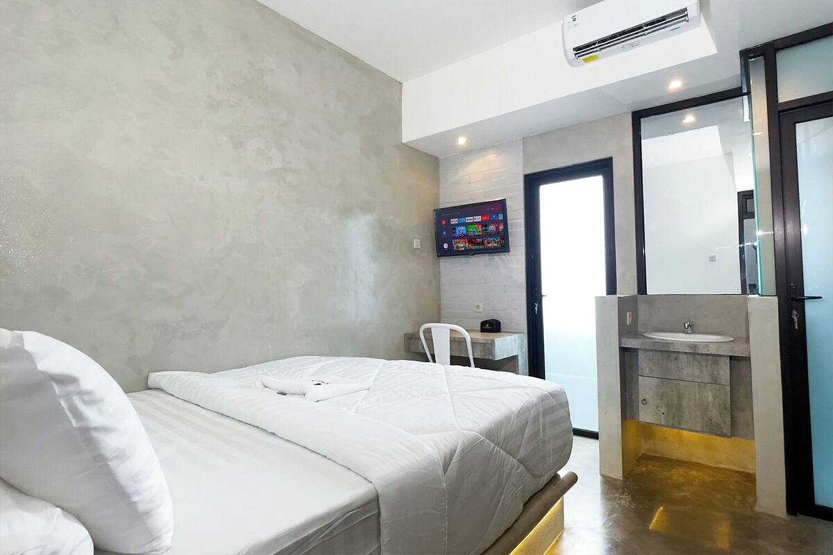Une chambre d’hôtel moderne équipée d’un lit, d’un petit bureau, d’une télévision et d’une salle de bain avec un lavabo et un miroir.