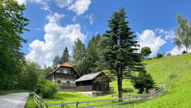 Una casa de campo con techo inclinado, cerca de madera y un paisaje verde exuberante.