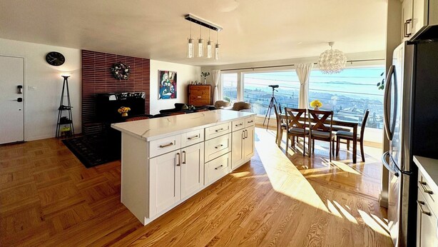 A modern kitchen with a central island, wooden flooring, and a dining area with a view. - Spacious 4BR Ocean‑View Home • Modern Kitchen • Near Beach & SF (Daly City)
