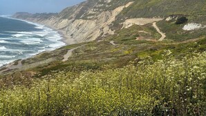 A coastal landscape with a dirt path leading to a beach, surrounded by hills and sparse vegetation. - Spacious 4BR Ocean‑View Home • Modern Kitchen • Near Beach & SF (Daly City)
