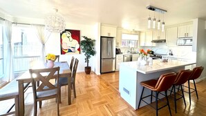 A modern kitchen with a large island, wooden flooring, and white cabinetry. - Spacious 4BR Ocean‑View Home • Modern Kitchen • Near Beach & SF (Daly City)