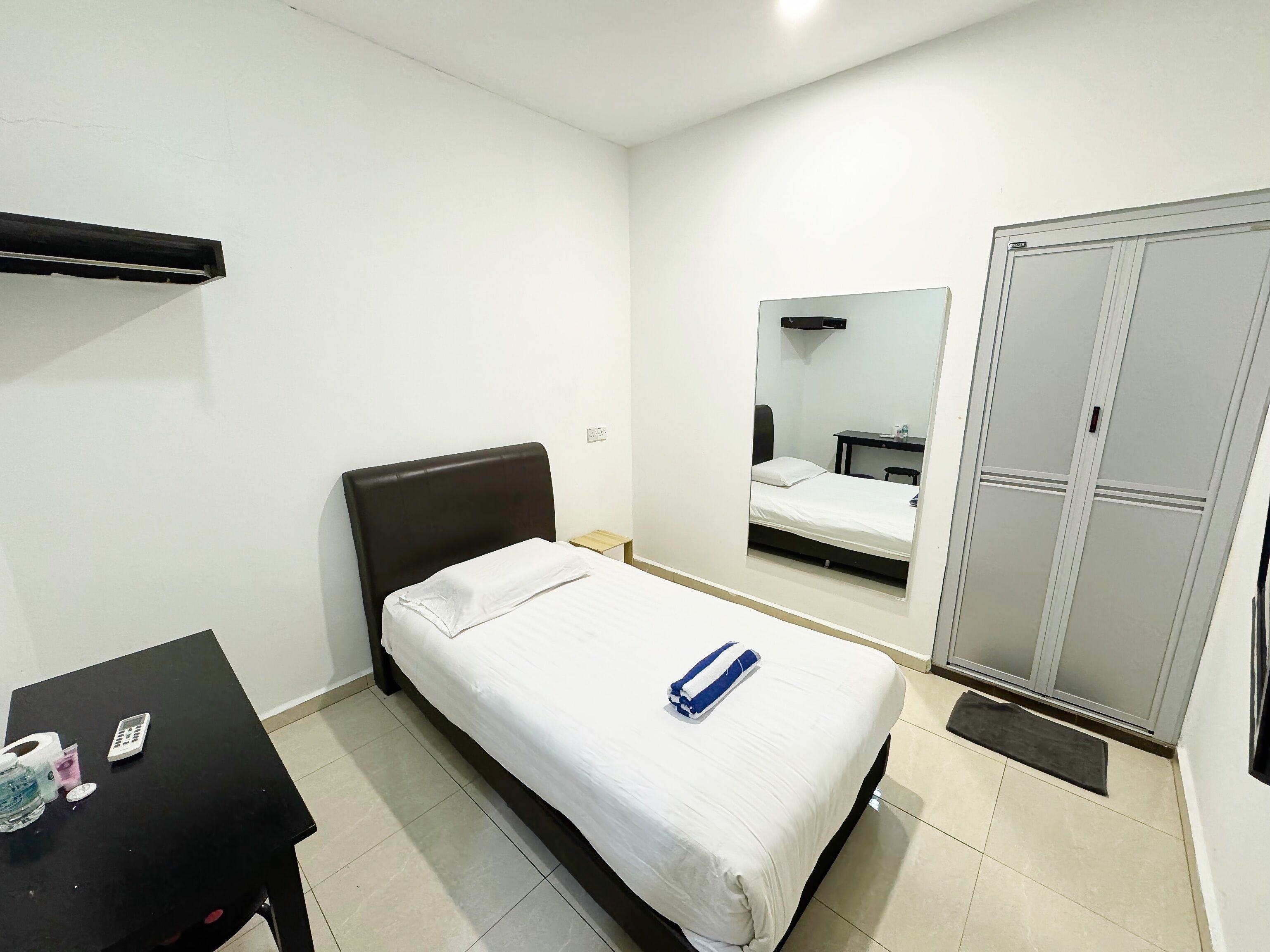 A bedroom with a single bed, a small table with a calculator, a water bottle, and a mirror on the wall.