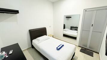 A bedroom with a single bed, a small table with a calculator, a water bottle, and a mirror on the wall.