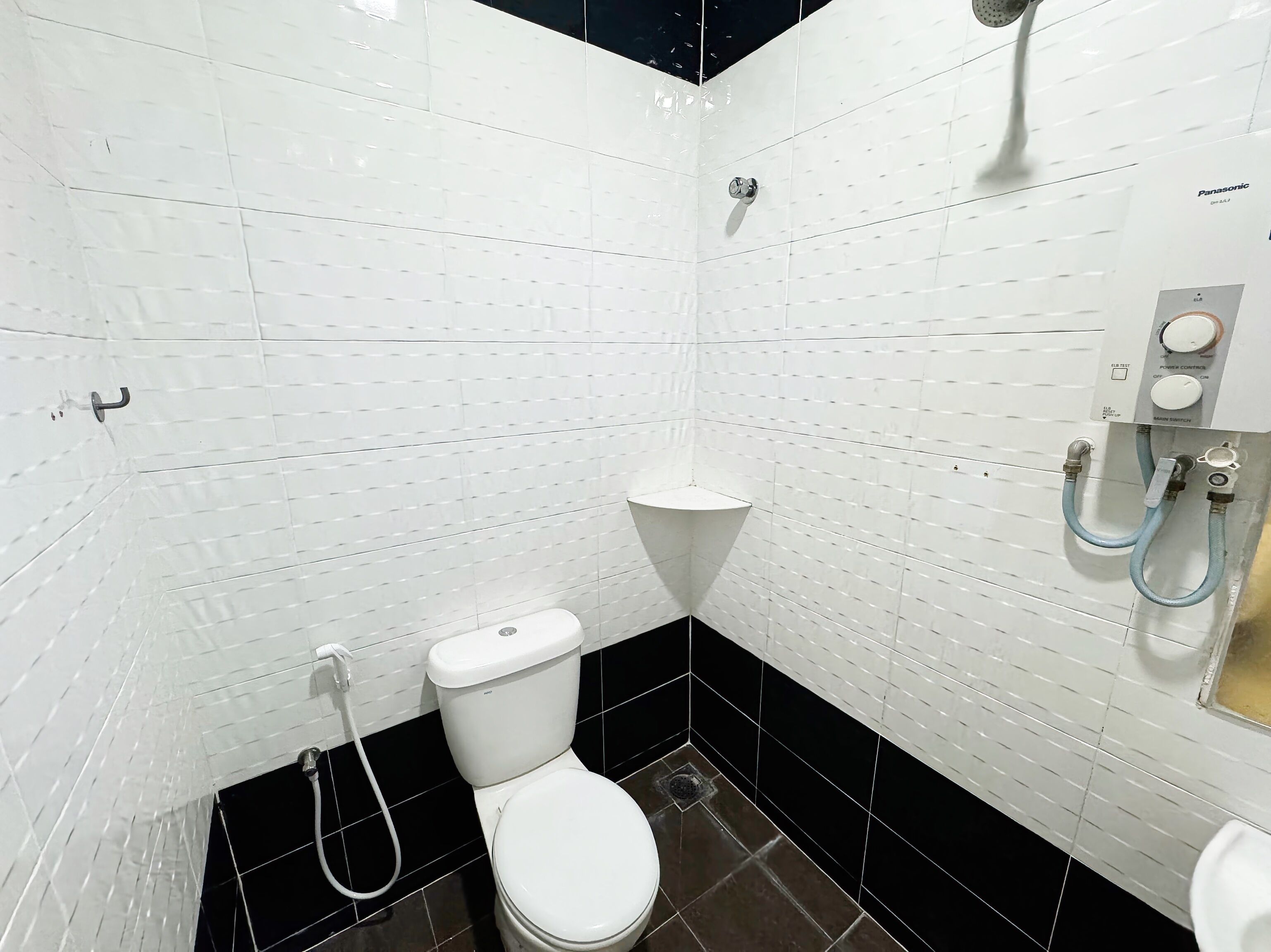 Une salle de bain avec des murs carrelés de blanc, des toilettes blanches, un sol carrelé de noir et une douche équipée d’un panneau de commande.