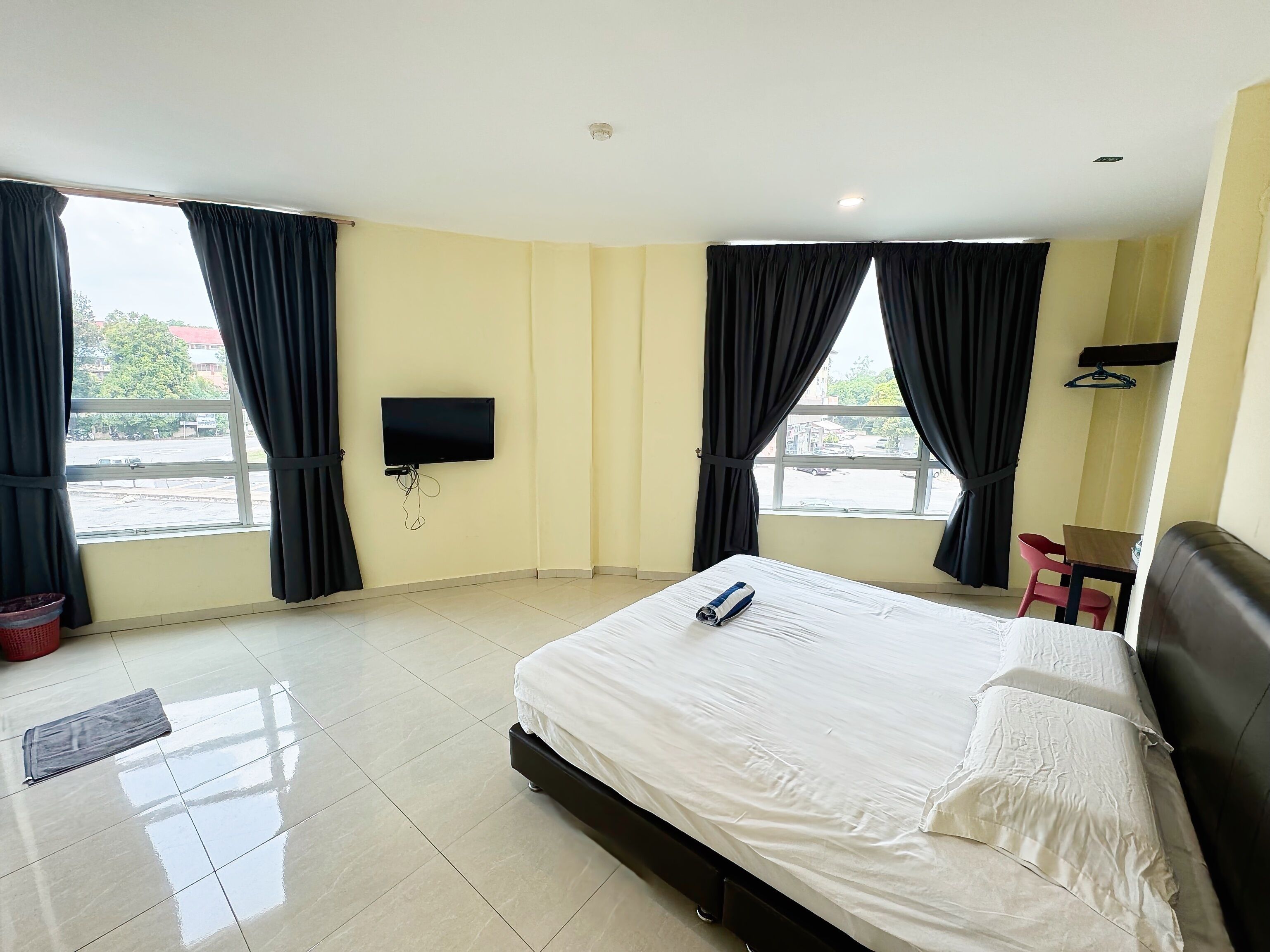 Habitación de hotel con una cama grande, un televisor de pantalla plana en la pared y una ventana con cortinas.