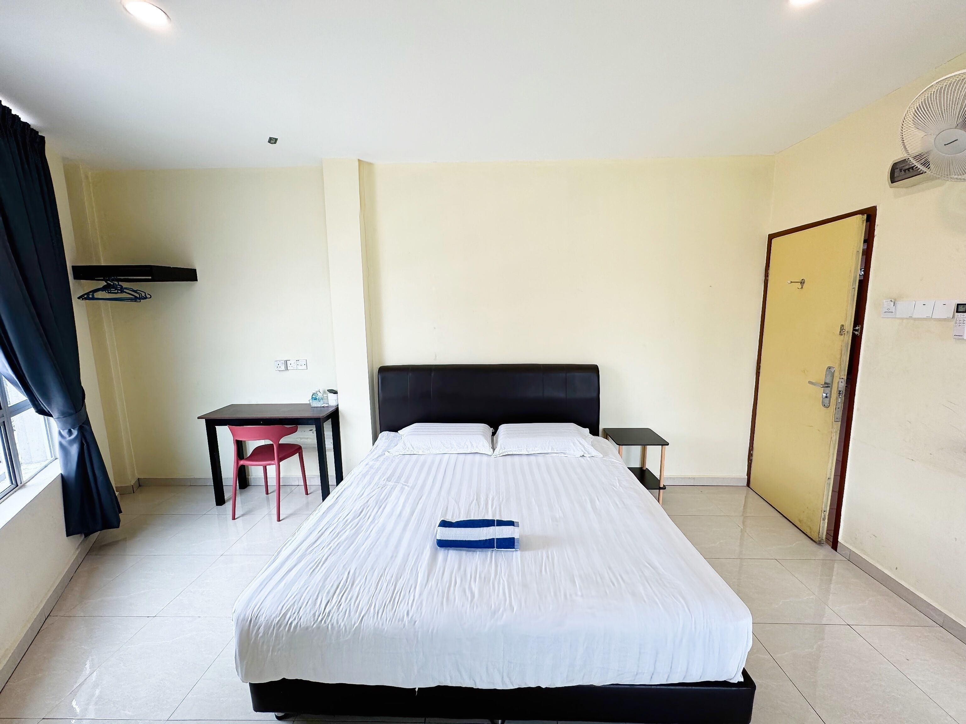 A hotel room with a bed, a desk, a chair, a small table, and a door.