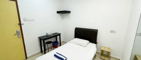 Una stanza piccola e pulita con un letto, una scrivania, una sedia, un cestino e una porta.