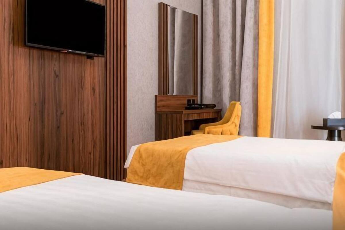 A hotel room with two beds, a TV mounted on the wall, a wooden panel wall, and a mirror.