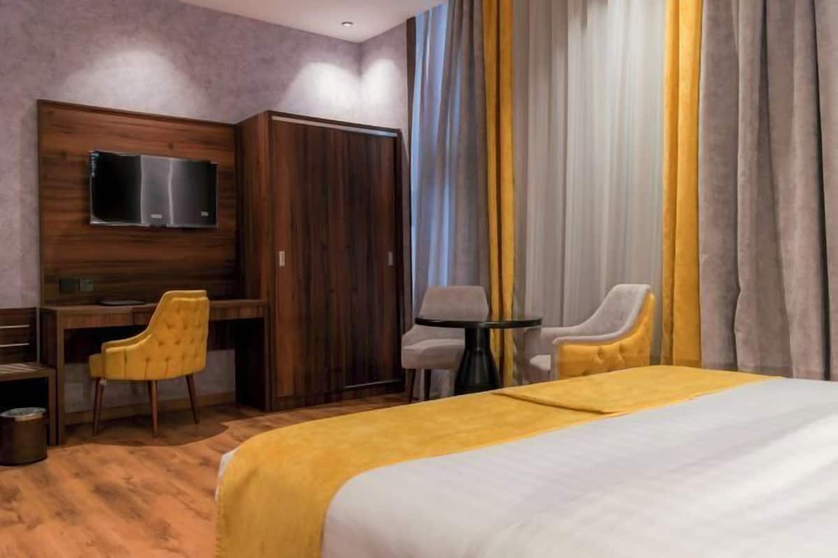 A hotel room with a bed, a desk, a chair, a television, and a wardrobe.