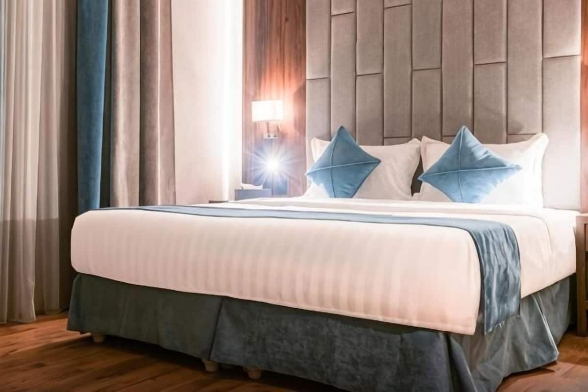 A hotel room with a large bed, a nightstand with a lamp, and a view of the outdoors.