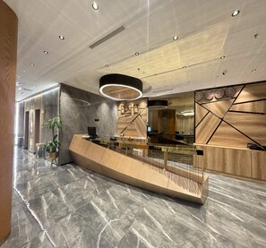 A modern reception area with a marble floor, a curved reception desk, and a large mirror. - Sunday MAS Hotel (Jeddah)