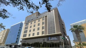 Un moderno edificio de hotel con fachada de vidrio, una entrada visible y un estacionamiento con varios coches.