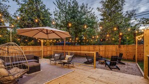 A wooden deck with outdoor furniture, including a hanging chair, sofas, and chairs, under string lights.