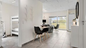 Una habitación moderna y bien iluminada con literas, una zona de comedor con sillas y una mesa, y un gran ventanal con vistas al exterior.