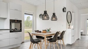 Una cocina moderna con armarios blancos, horno empotrado y comedor con mesa de madera y sillas negras.