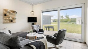 Una sala de estar moderna con un sofá gris, una mesa de centro redonda, un sillón de cuero negro y un televisor montado en la pared.
