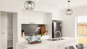 A modern kitchen with white cabinetry, a central island, and pendant lighting. - Modern Family Retreat in Premier GreenbankLocation (Greenbank)