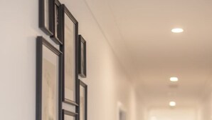 A hallway with framed pictures on the wall, a light-colored floor, and recessed ceiling lights. - Modern Family Retreat in Premier GreenbankLocation (Greenbank)