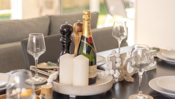 A dining table set with plates, glasses, a bottle of champagne, and candles. - Modern Family Retreat in Premier GreenbankLocation (Greenbank)