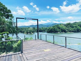 Una terraza de madera con un letrero del Hotel Mizu Tsuki que da a un río, con abundante vegetación y colinas al fondo.