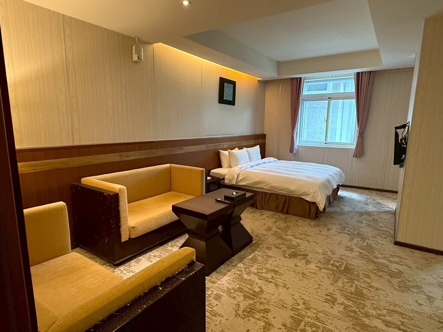 A hotel room with a bed, two sofas, a small table, and a window with curtains.